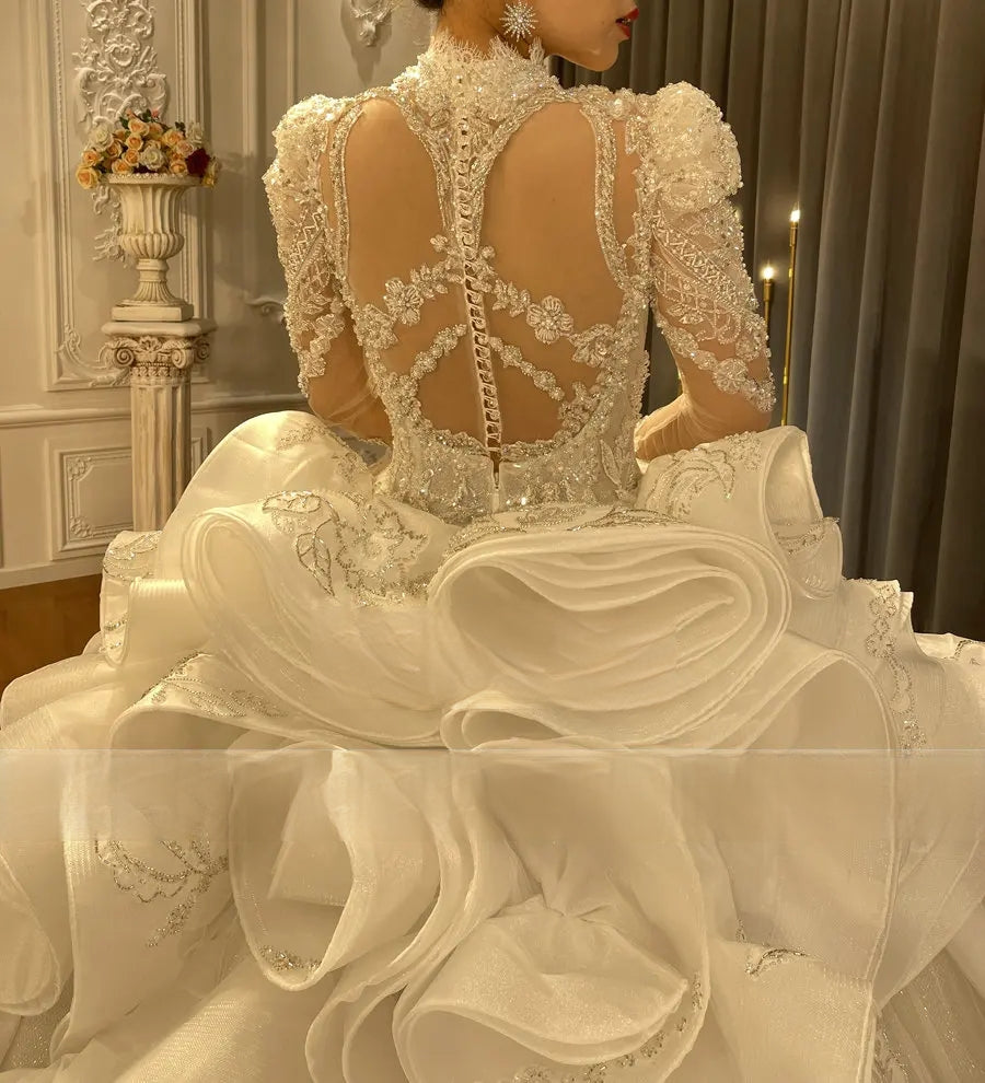 Close-up of an ornate beaded wedding dress back featuring a high lace collar, intricate crystal patterns, and voluminous architectural ruffled waist detail.