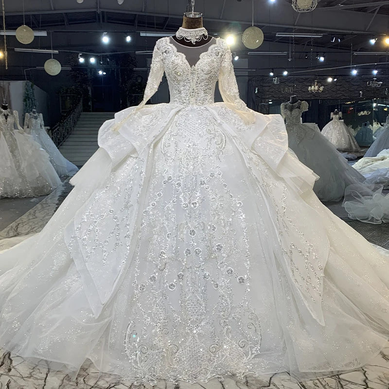 Front showroom view of a princess lace ball gown wedding dress on a mannequin, highlighting the sheer long sleeves and heavily beaded high O-neck collar.