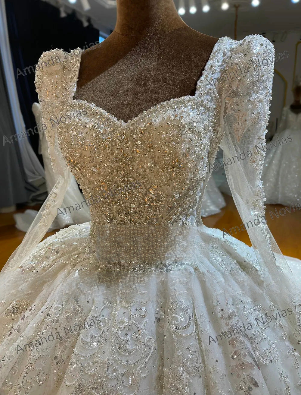 Close-up detail of a luxury bridal bodice with full sleeves, emphasizing the exquisite square neckline, dense silver crystal embroidery, and sparkling lace appliqués.