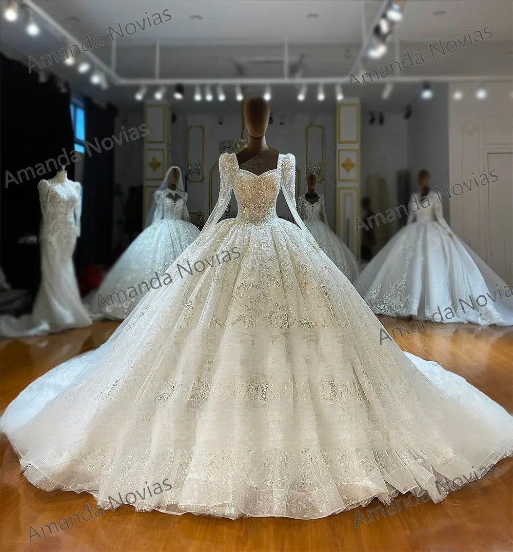 Angled front view of an exquisite long-sleeve wedding gown on a mannequin, showcasing the massive scale of the sparkling ball gown skirt and the intricate bodice details in a bridal boutique.