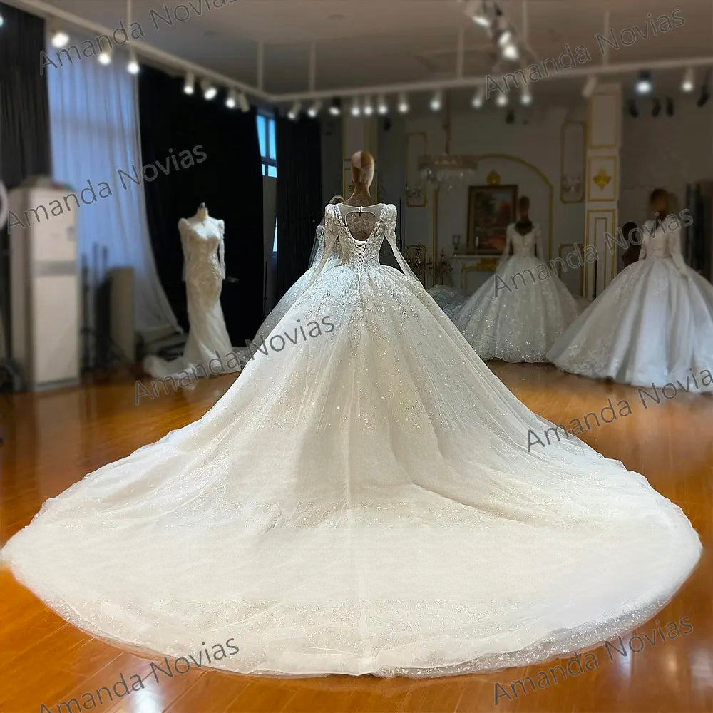 Detailed rear view of a luxury bridal ball gown highlighting the expansive shimmering tulle train, sheer keyhole back paneling, and traditional lace-up corset closure.