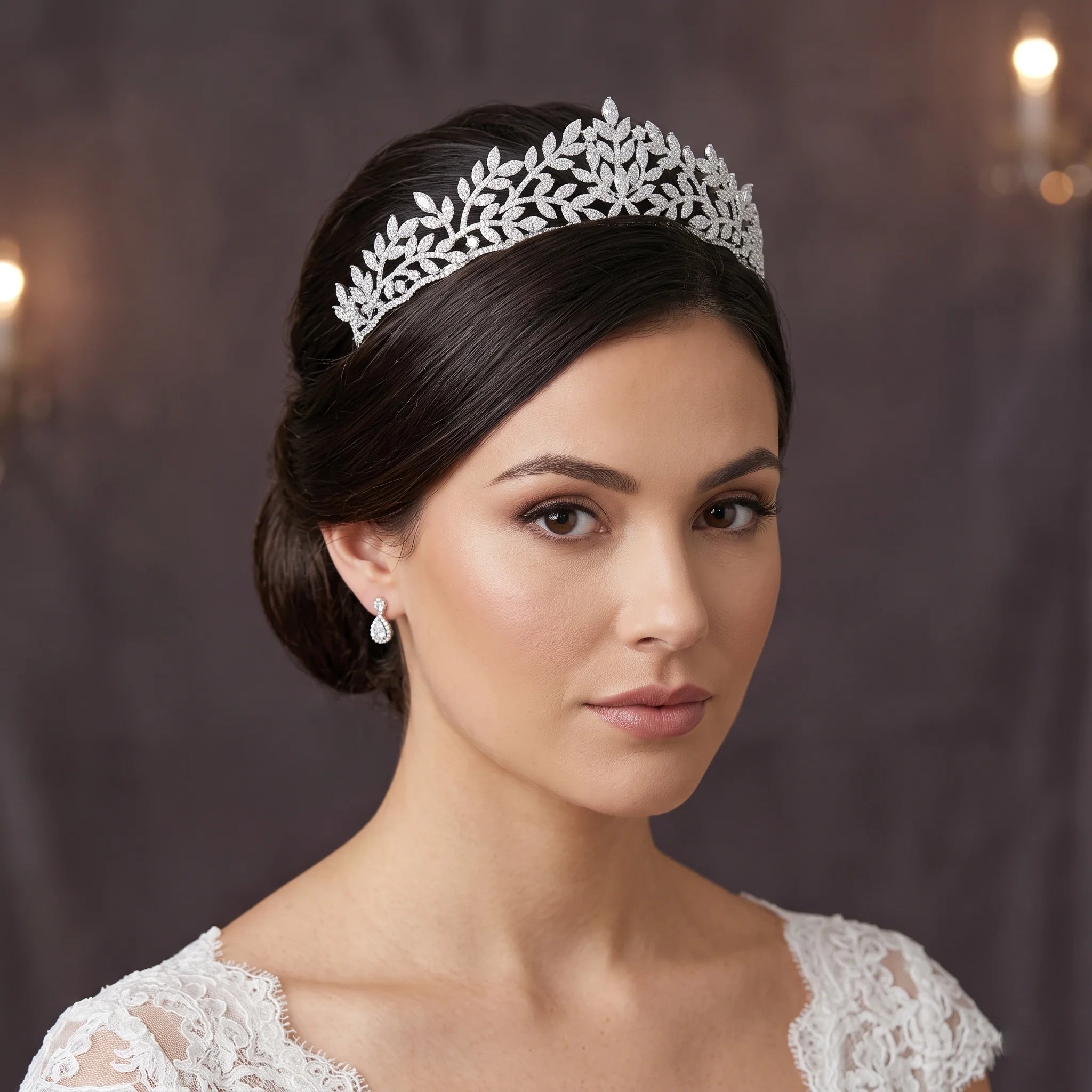 Headshot portrait of a brunette bride with a classic low bun hairstyle wearing a high-quality cubic zirconia leaf bridal wedding tiara crown and small matching drop earrings.