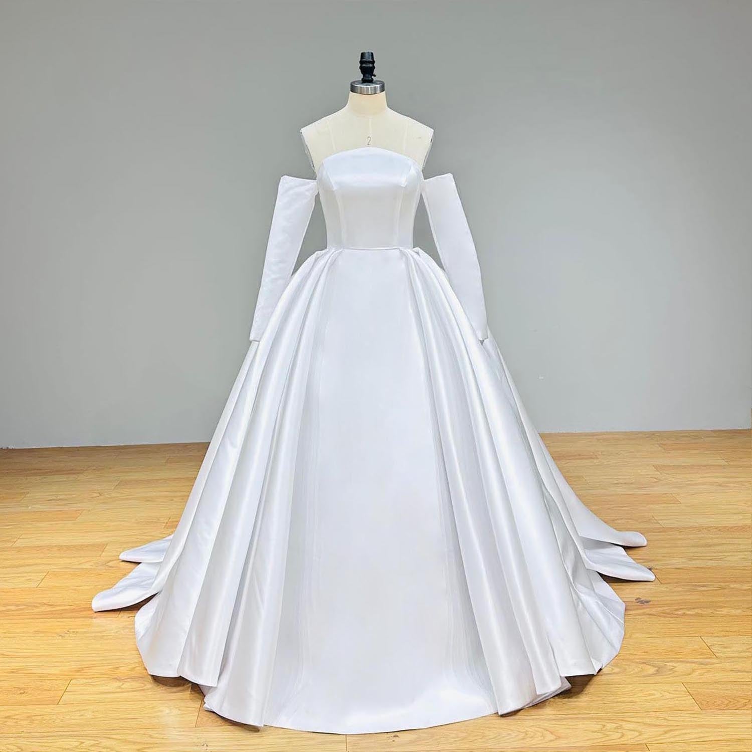 Wide front studio view of a high quality satin ball gown wedding dress on a mannequin, featuring a smooth, minimalist bodice and a dramatic pleated skirt with matching detached sleeves.