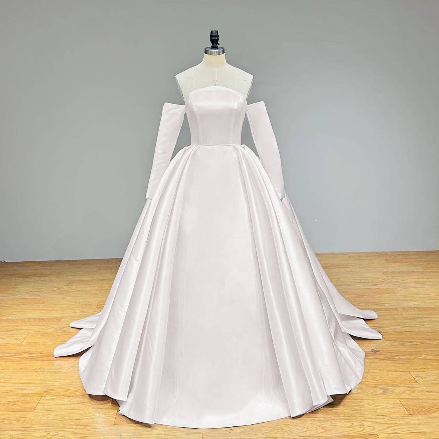 Elegant full front view of a light effect fashion gelinlik satin ball gown wedding dress on a mannequin, showcasing the pristine, high-quality fabric, straight neckline, and modern detached long sleeves.