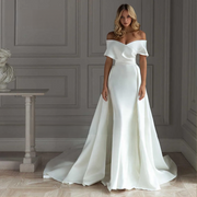 Front view of a model wearing a light effect satin mermaid wedding dress with an off-the-shoulder draped neckline and a majestic detachable train.