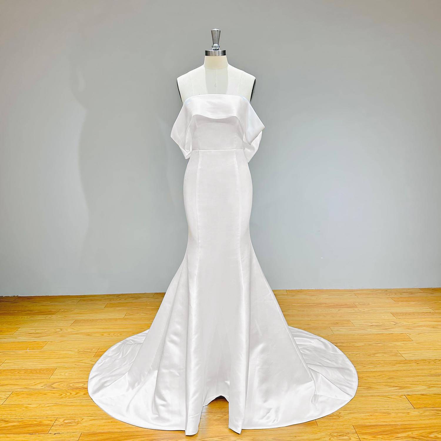 Full-length front view of a white liquid satin mermaid bridal gown on a mannequin, showcasing the structured strapless bodice with a draped off-shoulder cuff overlay.
