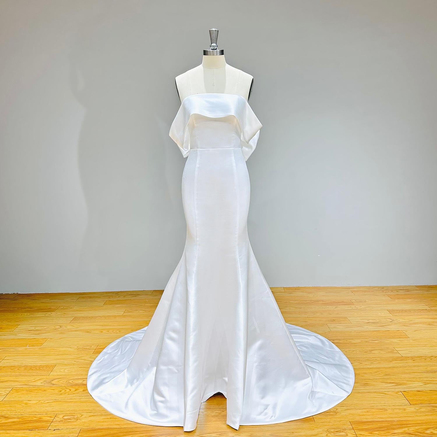 Front perspective of a simple heavy satin bridal dress on a mannequin against a solid gray background, highlighting the architectural tailored seams.