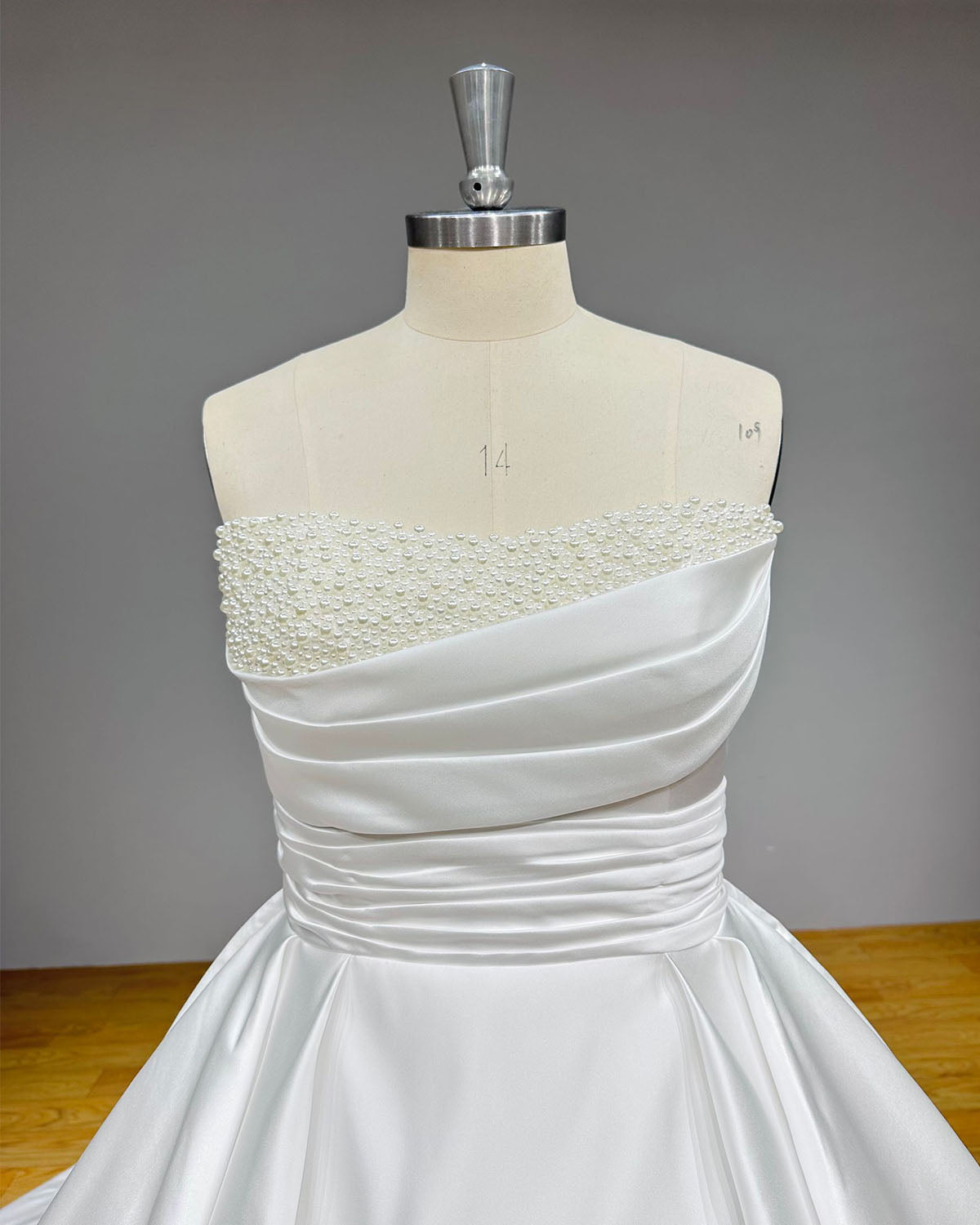 Detailed close-up of a structured bridal bodice showcasing precise diagonal fabric pleating and a sleek off-the-shoulder folded cuff design on a couture mannequin.