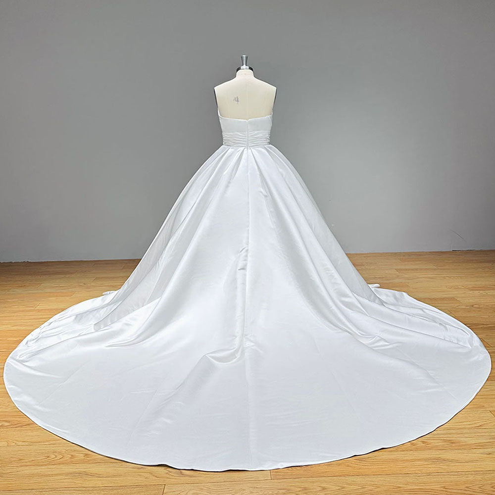 Studio back view of a minimalist satin wedding dress on a mannequin, showcasing a low straight back cut, a neat zipper closure, and an expansive chapel-length train.