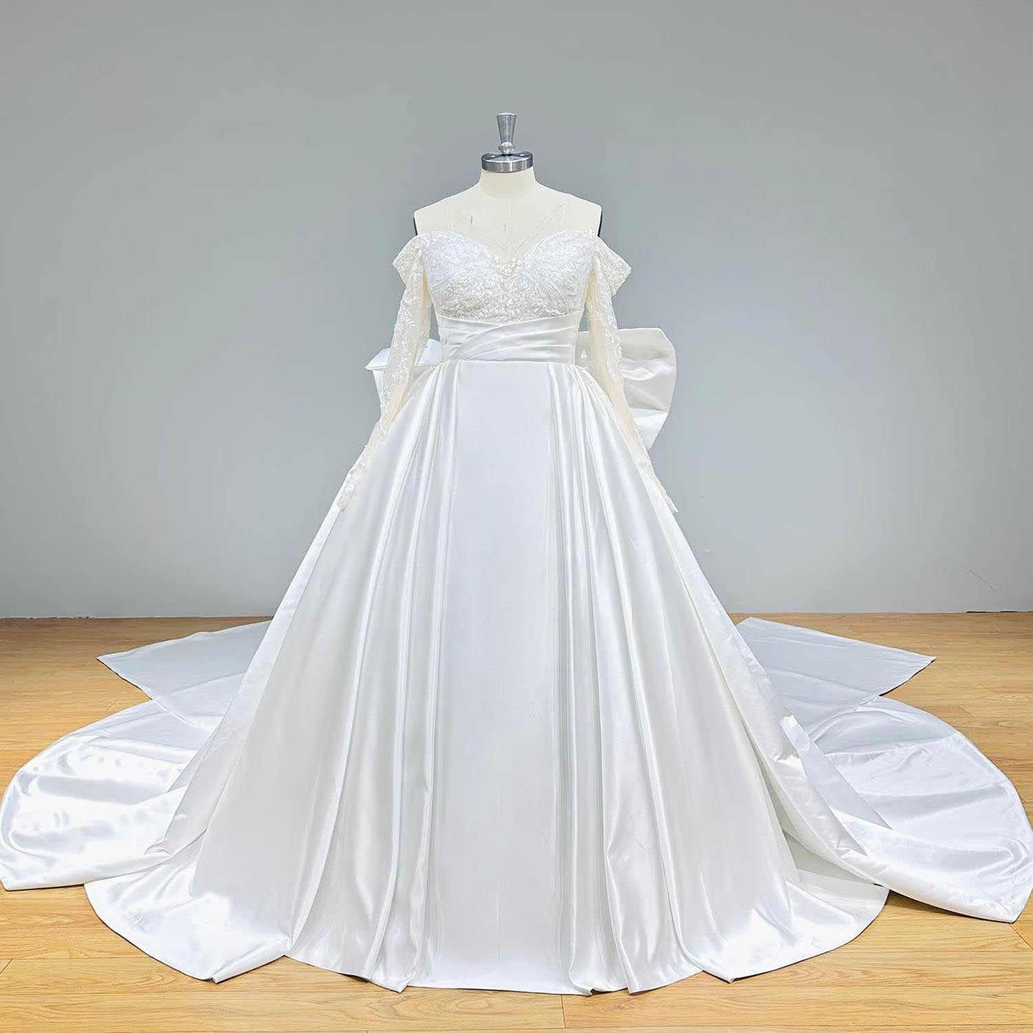 Clean studio front view of a light effect satin wedding dress on a mannequin, featuring a beautifully draped satin waist, an off-shoulder lace sweetheart bodice, and a flowing chapel train.
