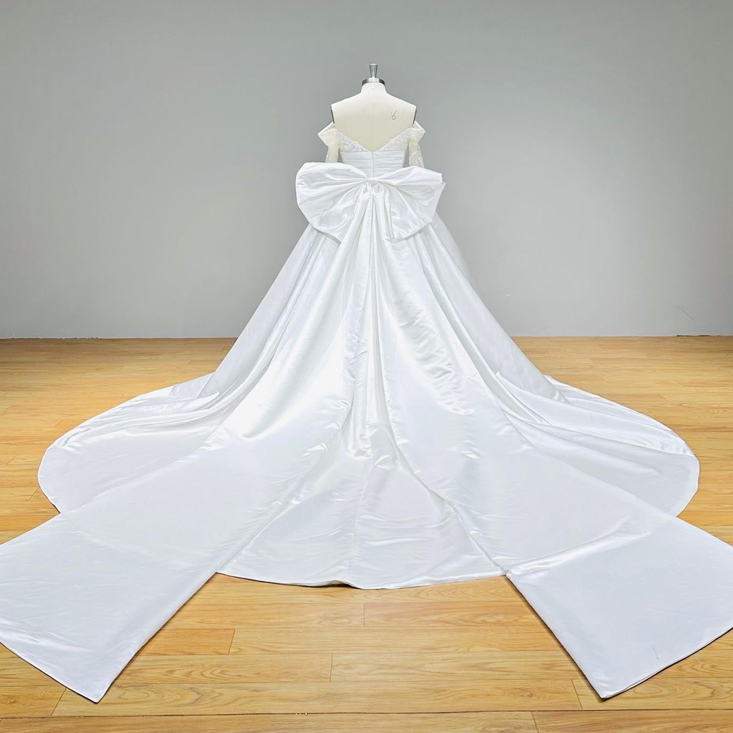 Dramatic full back view of an elegant satin wedding gown on a mannequin, displaying the voluminous detachable big bow and a wide, perfectly spread light effect chapel train.