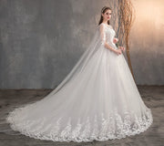 Elegant wedding dress with a long, sheer lace cape, intricate embroidery, and a voluminous tulle skirt with a train.
