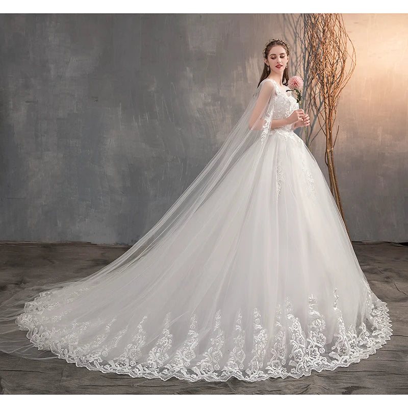 A bride wearing a sophisticated white wedding gown featuring a sheer lace cape, floral embroidery, and a grand, sweeping train.