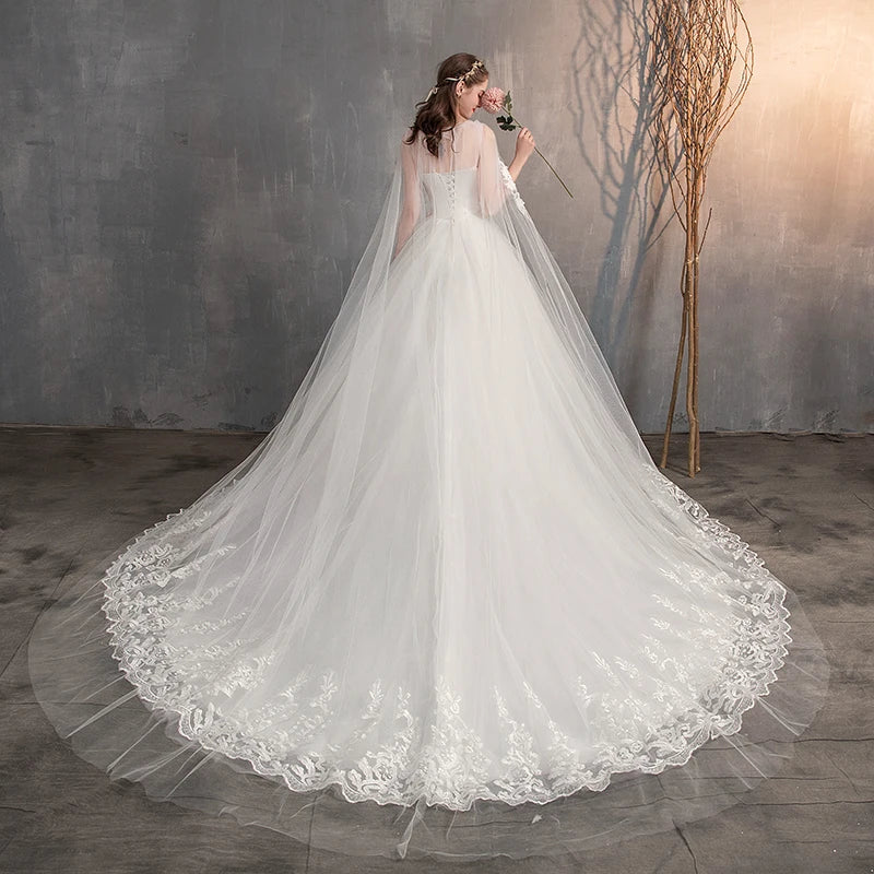 The back view of a white bridal gown, highlighting a long, delicate sheer lace cape and an expansive, lace-trimmed train.