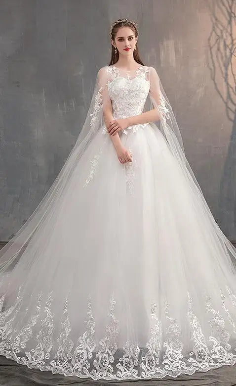 Elegant white bridal dress featuring a sheer lace cape, intricate embroidery on the skirt, and a long train for a classic wedding look.