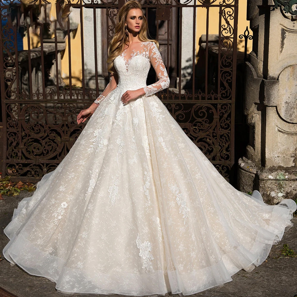 A model wearing an elegant long sleeve A-line wedding dress with illusion lace detailing and delicate floral appliques.