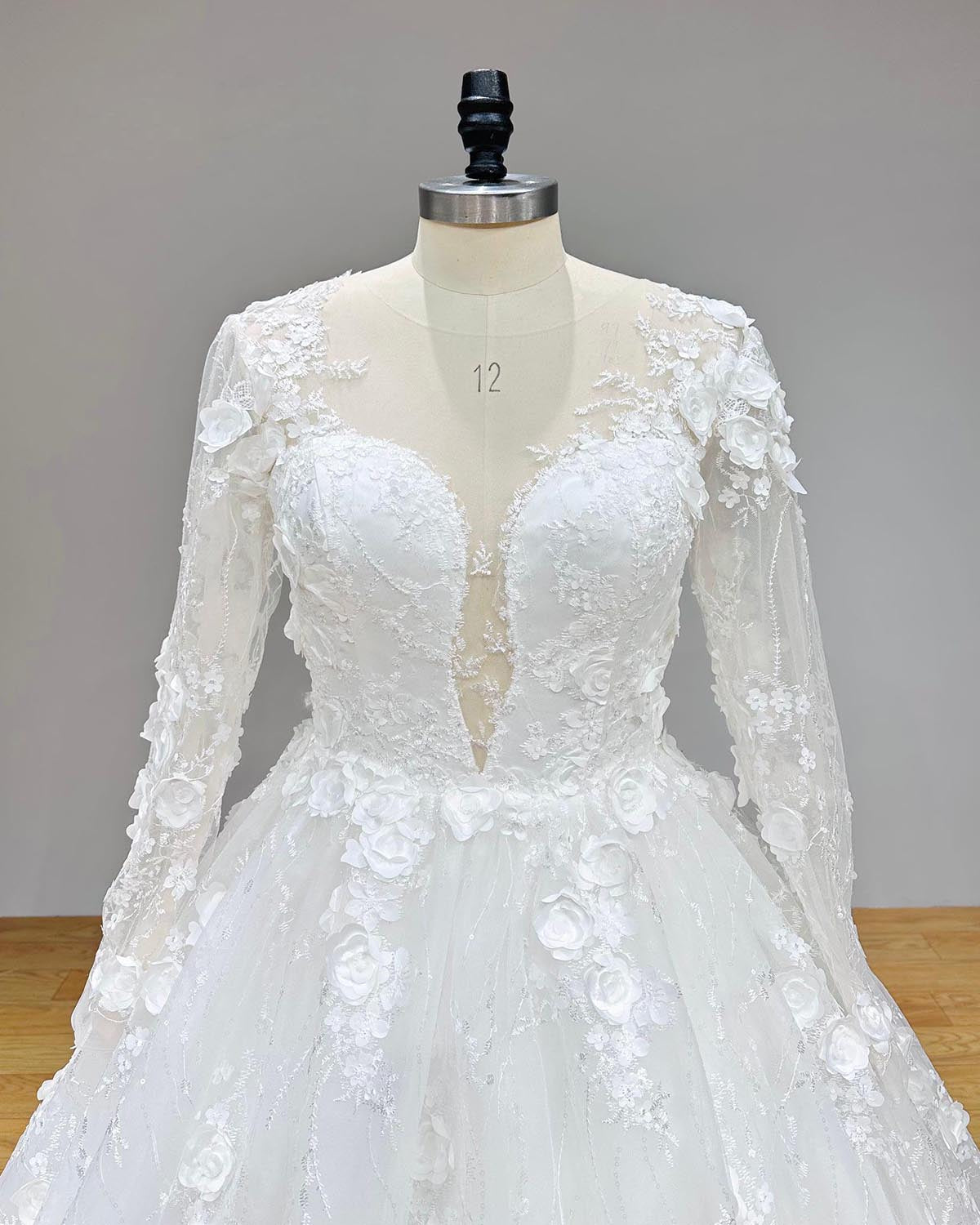 Close-up detail of the long-sleeve bodice featuring intricate floral lace embroidery and sheer illusion neckline on a bridal ball gown.