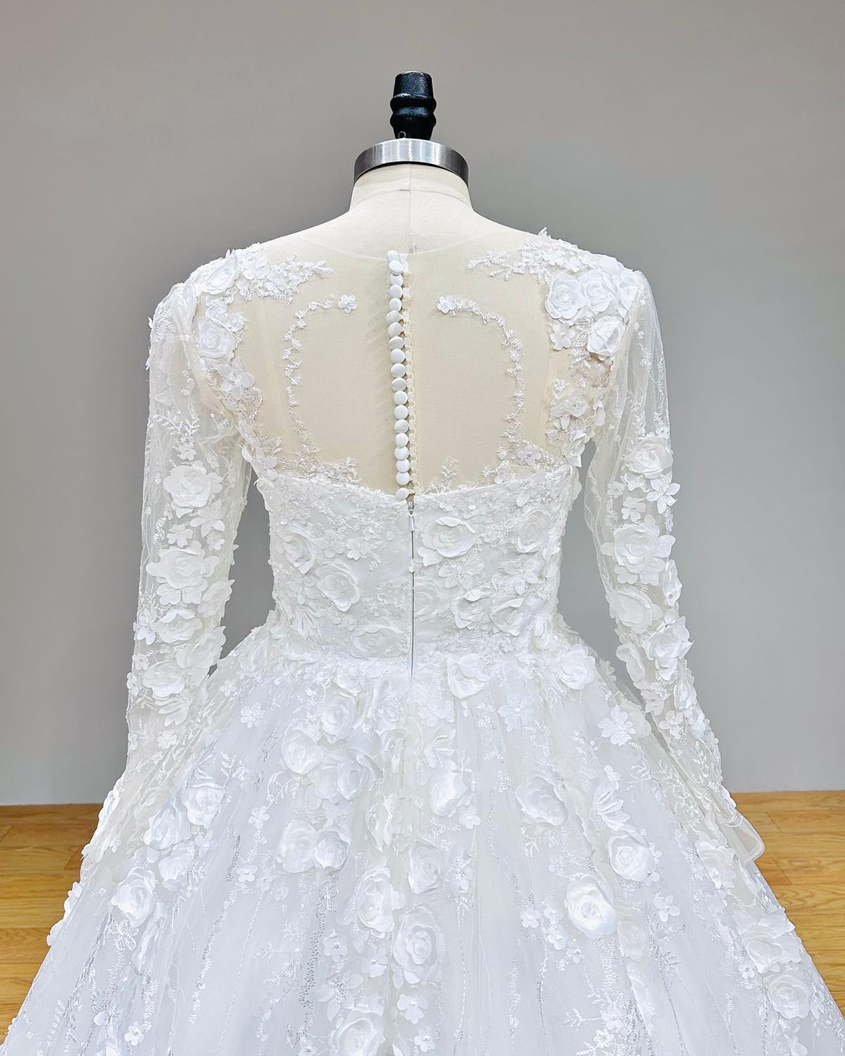 Detailed back view of a long-sleeve wedding dress showcasing the delicate button closure and intricate floral lace illusion back.