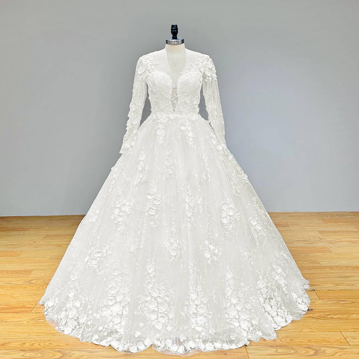 Front view of a white long-sleeve floral ball gown wedding dress with a voluminous skirt and detailed lace appliques on a mannequin.