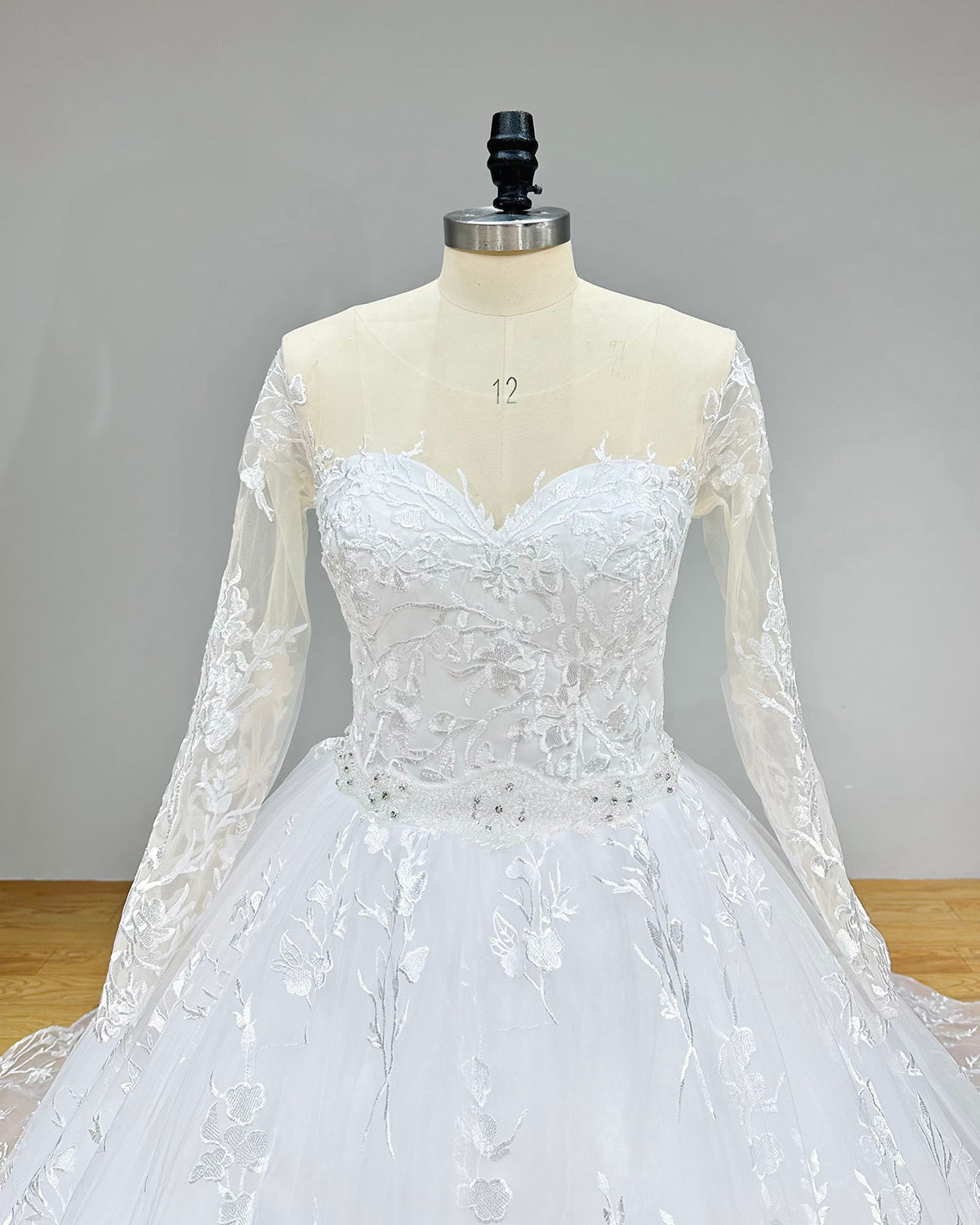 Close-up back bodice detail of a wedding gown on a mannequin, showcasing the unique cut-out back design, sheer lace detailing, and fine button closures above the crystal beading belt.
