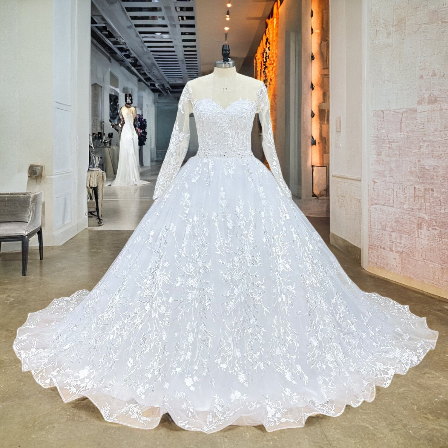 Plus-size bridal model in a luxury gallery setting modeling a long sleeve ball gown wedding dress with a cinched crystal beading belt and a sophisticated cut-out back.