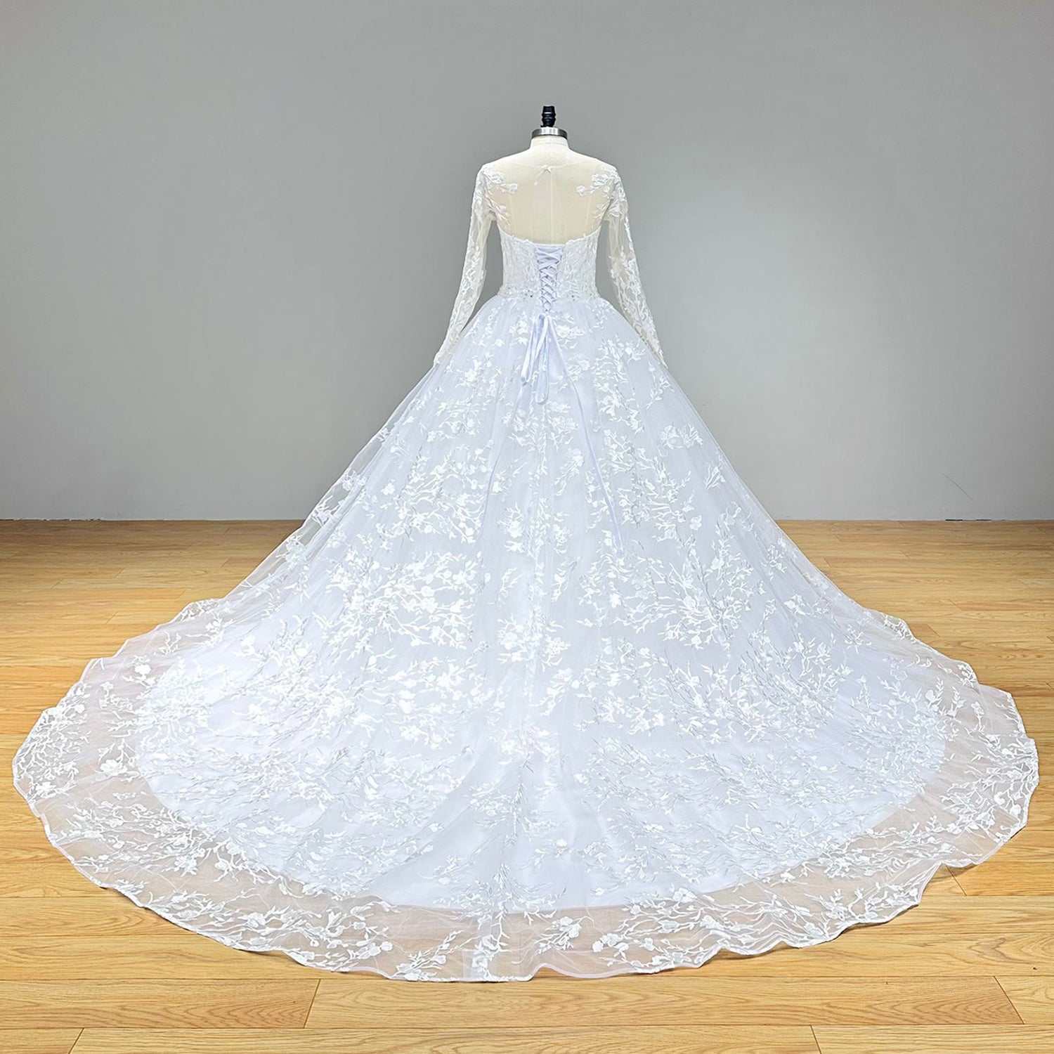 Close-up front bodice detail of a ball gown wedding dress on a mannequin, emphasizing the smooth satin fabric, long fitted sleeves, and the sparkling crystal beading belt at the waist.