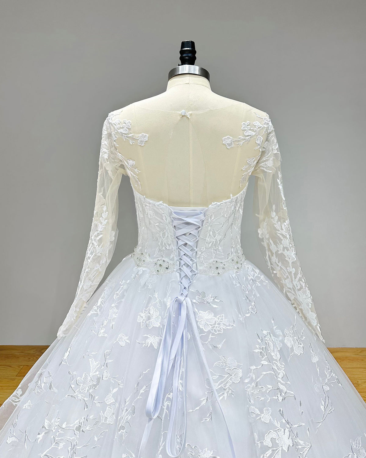 Dramatic full back view of a long sleeve ball gown wedding dress on a mannequin, perfectly displaying the elegant cut-out back, button accents, and a wide, sweeping bridal train.