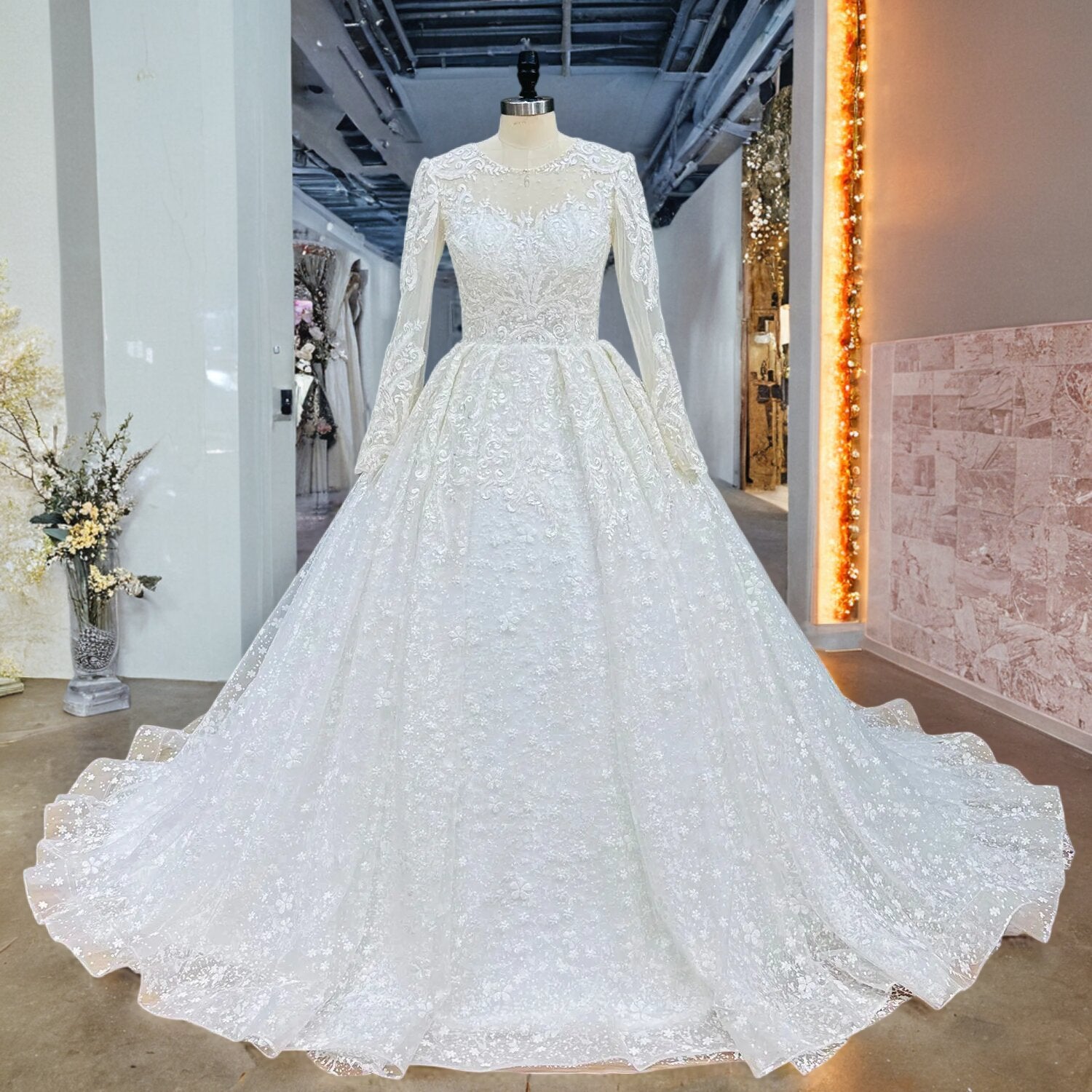 Front full-length view of a long sleeve bridal ball gown featuring detailed floral lace appliques on a showroom mannequin.