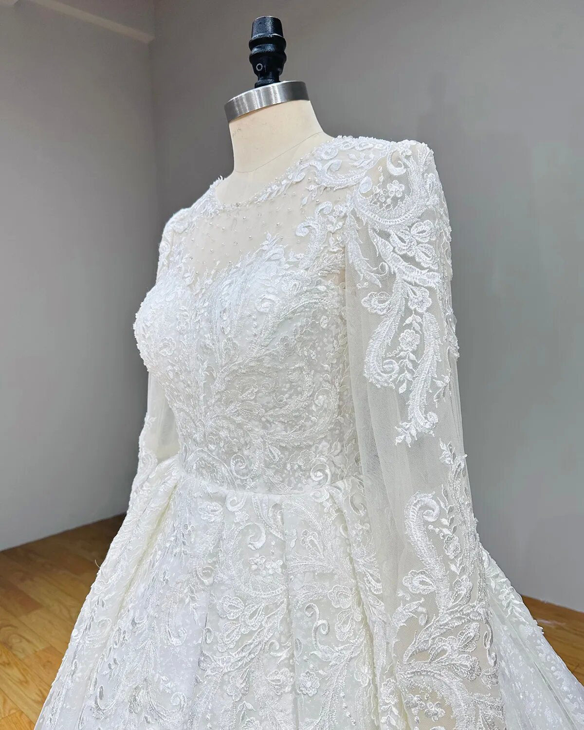 Close-up profile of a wedding dress bodice, showcasing intricate beaded floral appliques along a sheer long illusion sleeve.