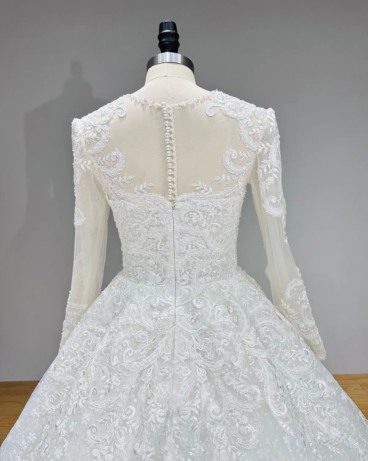 Detailed back view of a bridal gown showcasing a sheer illusion back with a neat line of satin-covered pearl buttons.