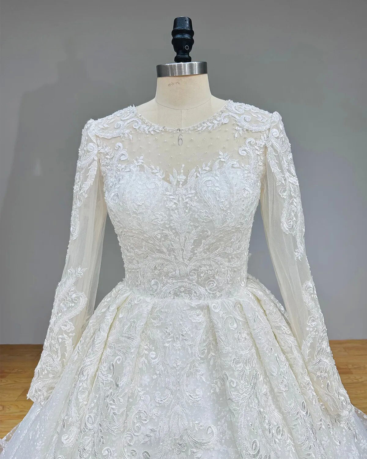 Close-up front view of a wedding dress bodice featuring a sheer beaded illusion neckline and fine lace embroidery.