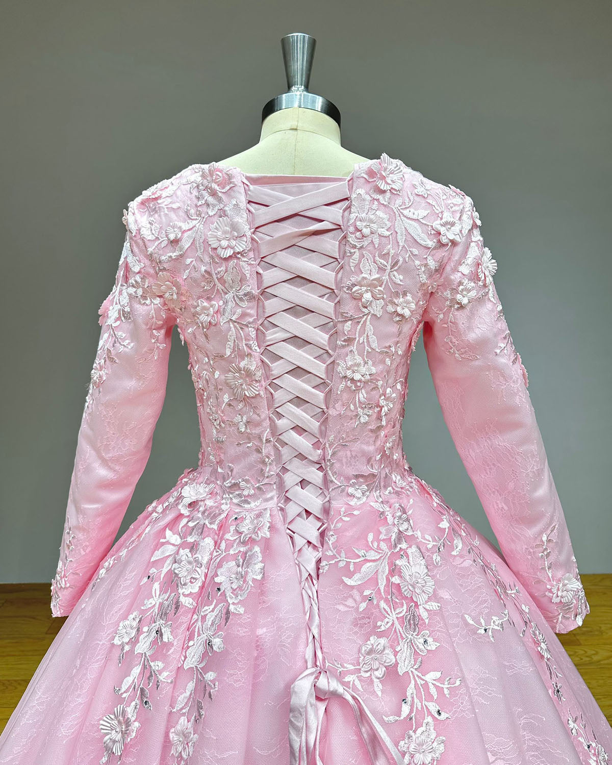 Close-up of the back of a pink bridal dress showing an adjustable satin lace-up corset closure surrounded by 3D floral lace appliques.