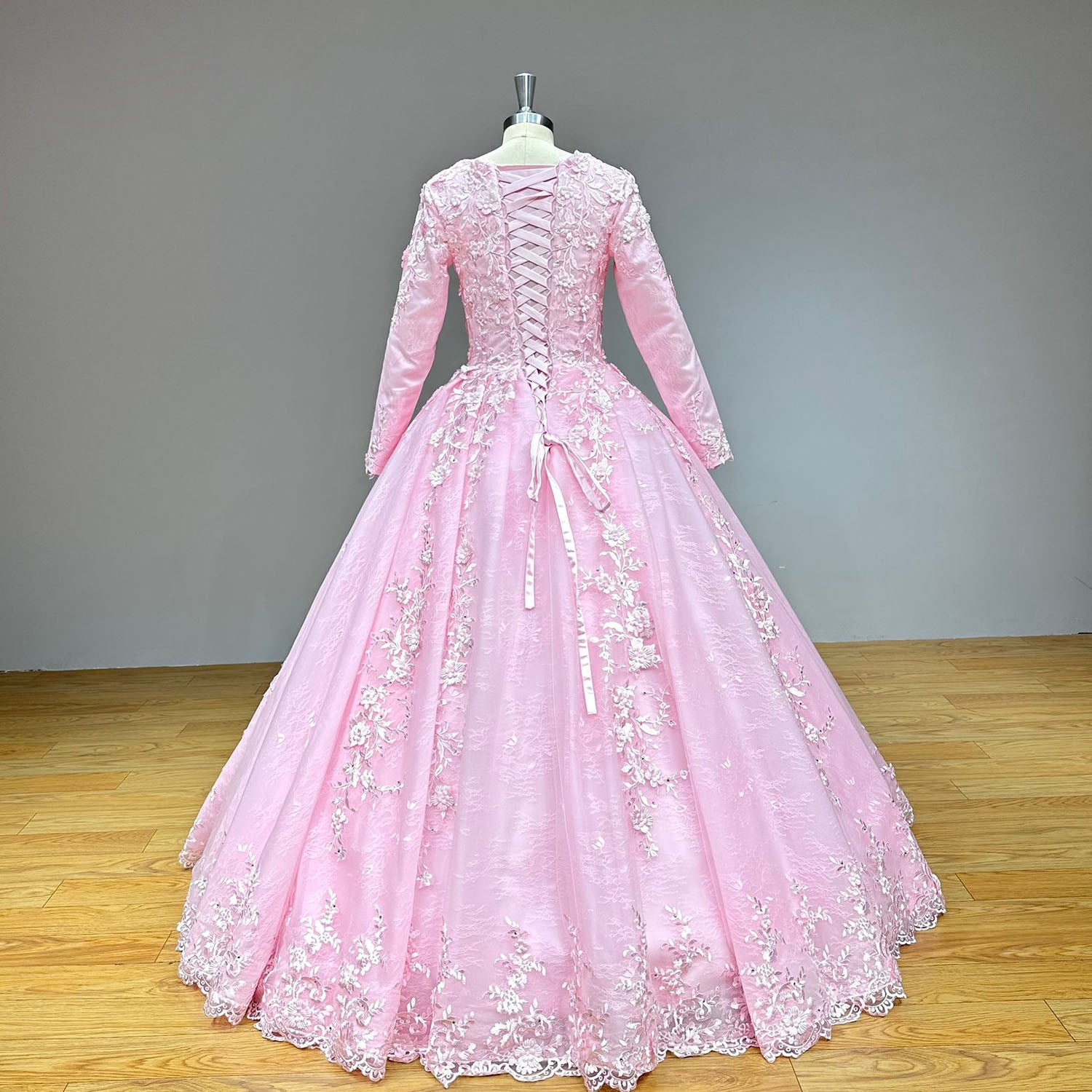 Full back view of a pink long-sleeve wedding dress highlighting a classic corset back design and a heavily decorated lace-bordered train.
