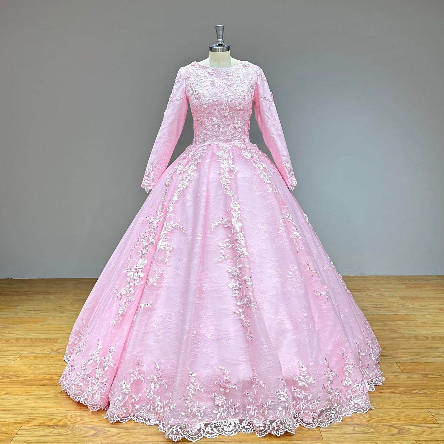 Front view of a pastel pink long-sleeve ball gown bridal gown with a crew neckline and a majestic A-line skirt on a dress form.