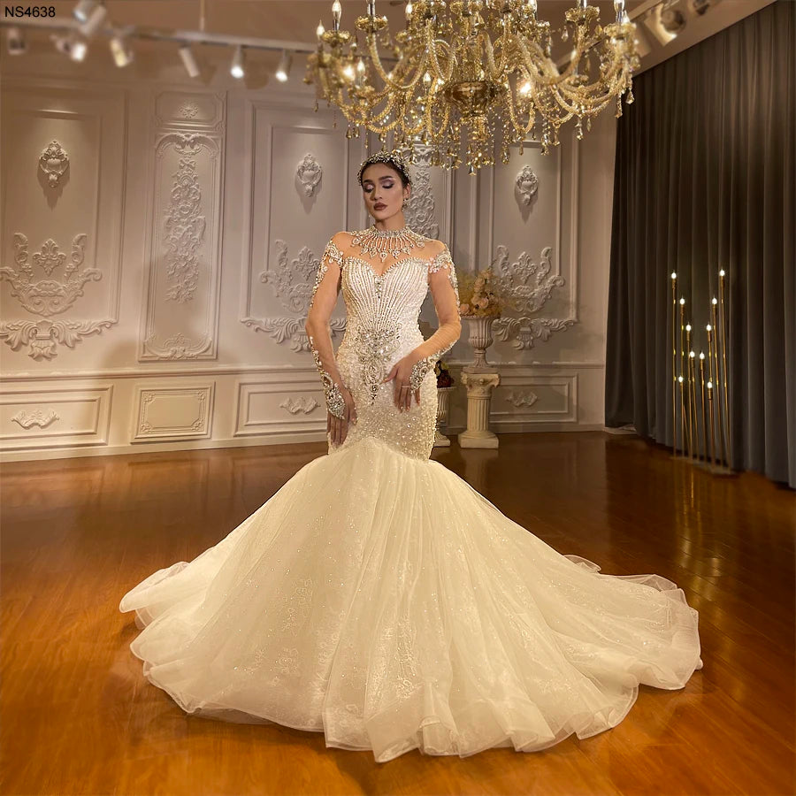 Full-length front view of a luxury long sleeve beaded mermaid bridal gown featuring an intricate crystalline bodice and a dramatic, voluminous ruffled tulle skirt.