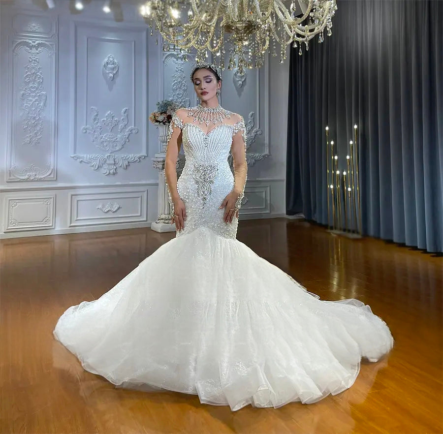Full-length shot of an off-white long sleeve beaded mermaid bridal gown with a structured embroidered bodice and an expansive flared bottom displayed in a luxury showroom setting.