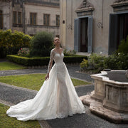 A bride posing in a luxurious long-sleeve mermaid wedding dress, featuring intricate beading, sequins, lace appliques, and a dramatic detachable train.