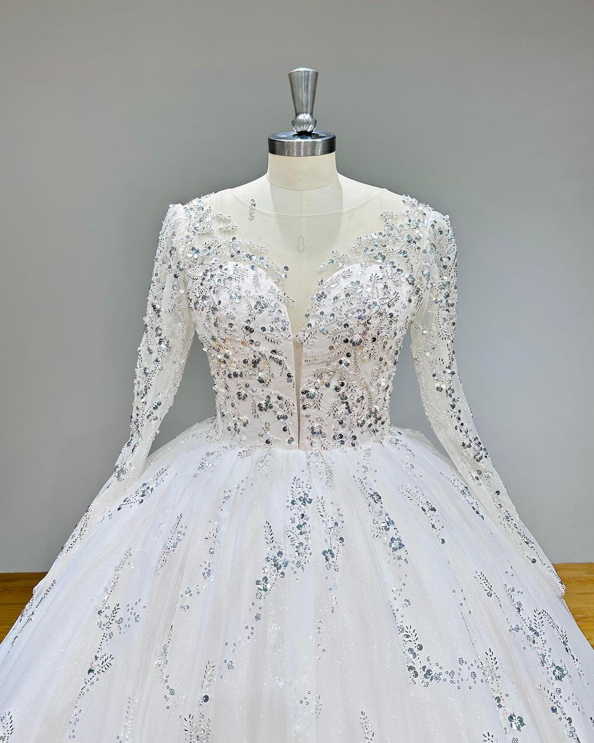 Close-up detail of the sequin-embellished bodice and illusion neckline on an elegant long-sleeve wedding gown.