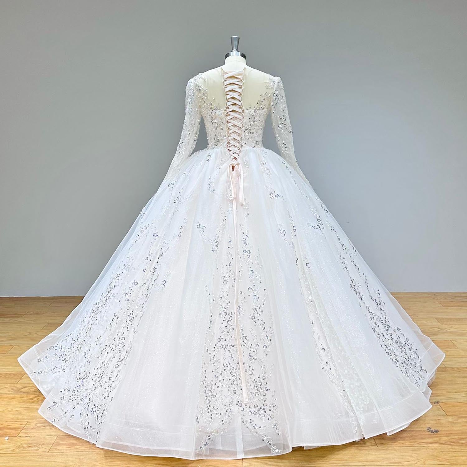 Back view of a long-sleeve ball gown wedding dress featuring a corset lace-up back and long train on a display mannequin.