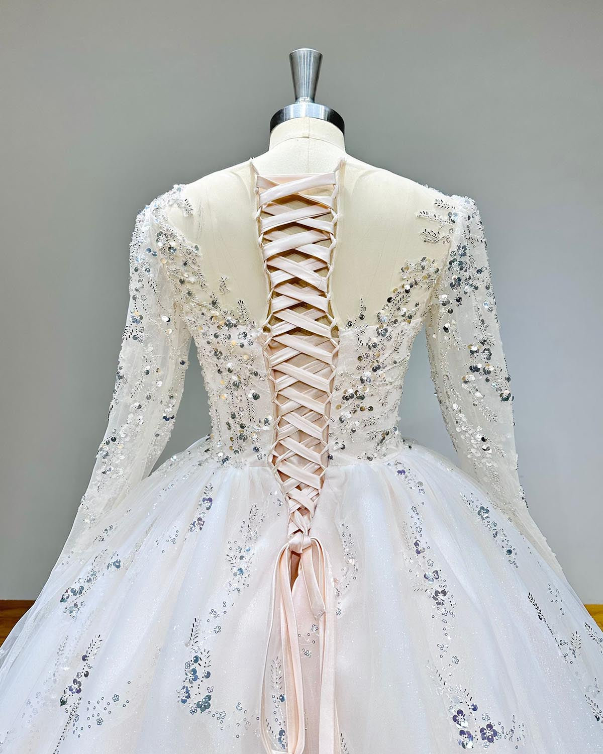 Detailed back view of the lace-up corset closure and long sleeves on a classic sequin-embellished wedding gown."