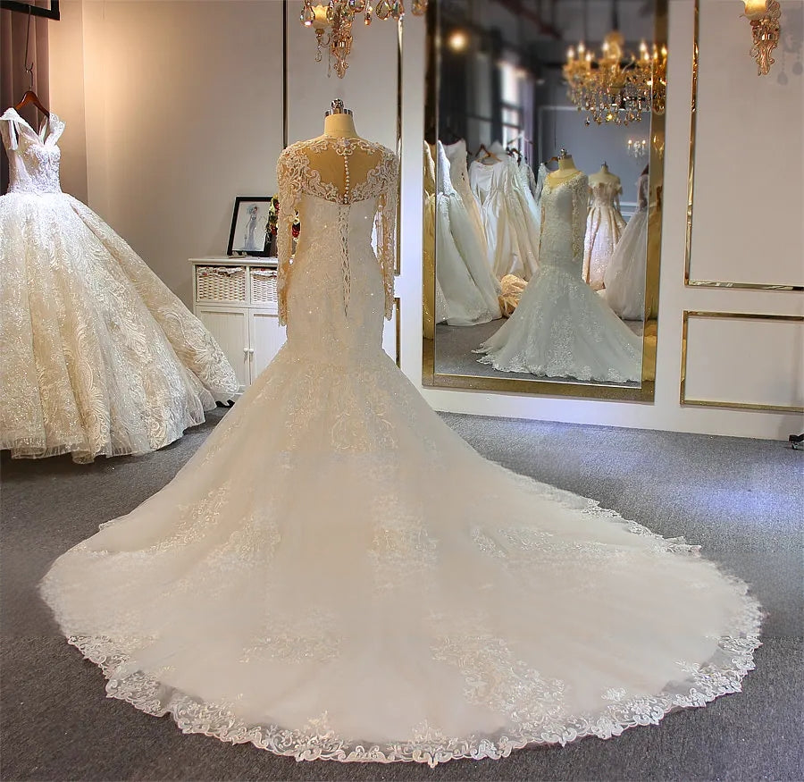 Full rear view of a long sleeve mermaid wedding dress on a mannequin, highlighting the dramatic extension of its expansive circular train with ornate lace embroidery.