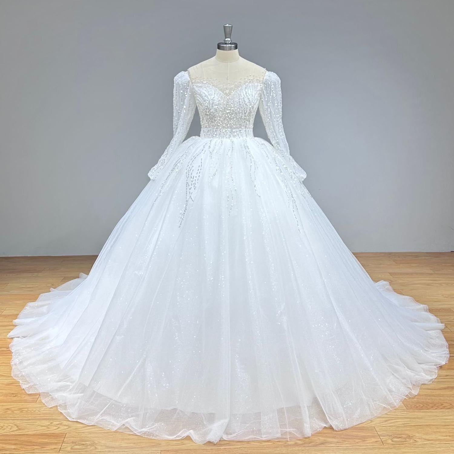 Studio front view of an elegant long sleeve glitter bridal gown on a mannequin, featuring intricate sequined beading across the bodice and sleeves.