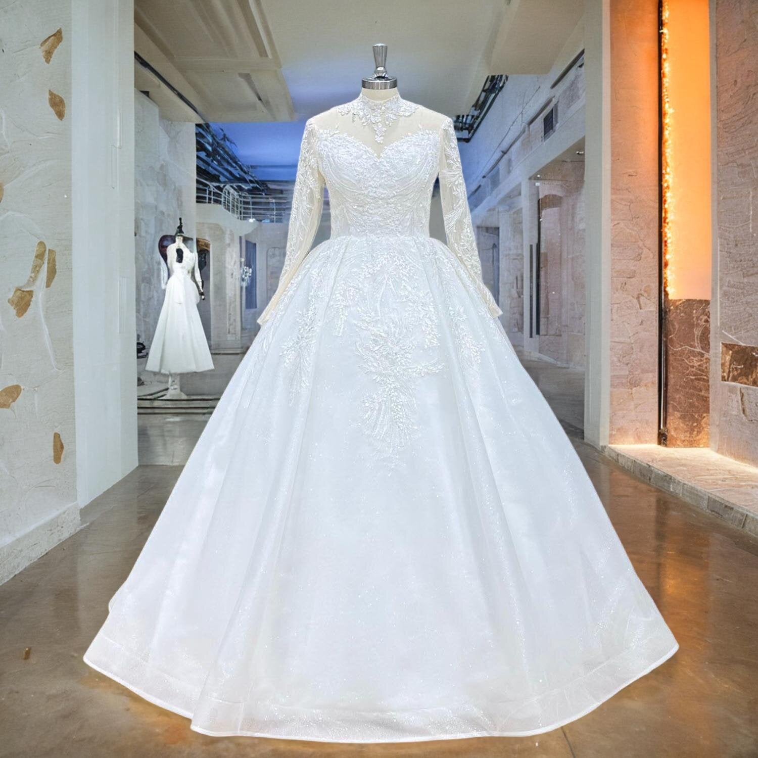 Front view of a luxury bridal gown on a mannequin, showcasing the long sleeve high neck silhouette, heavy sequined beadwork, and wide A-line skirt in a well-lit studio hallway.
