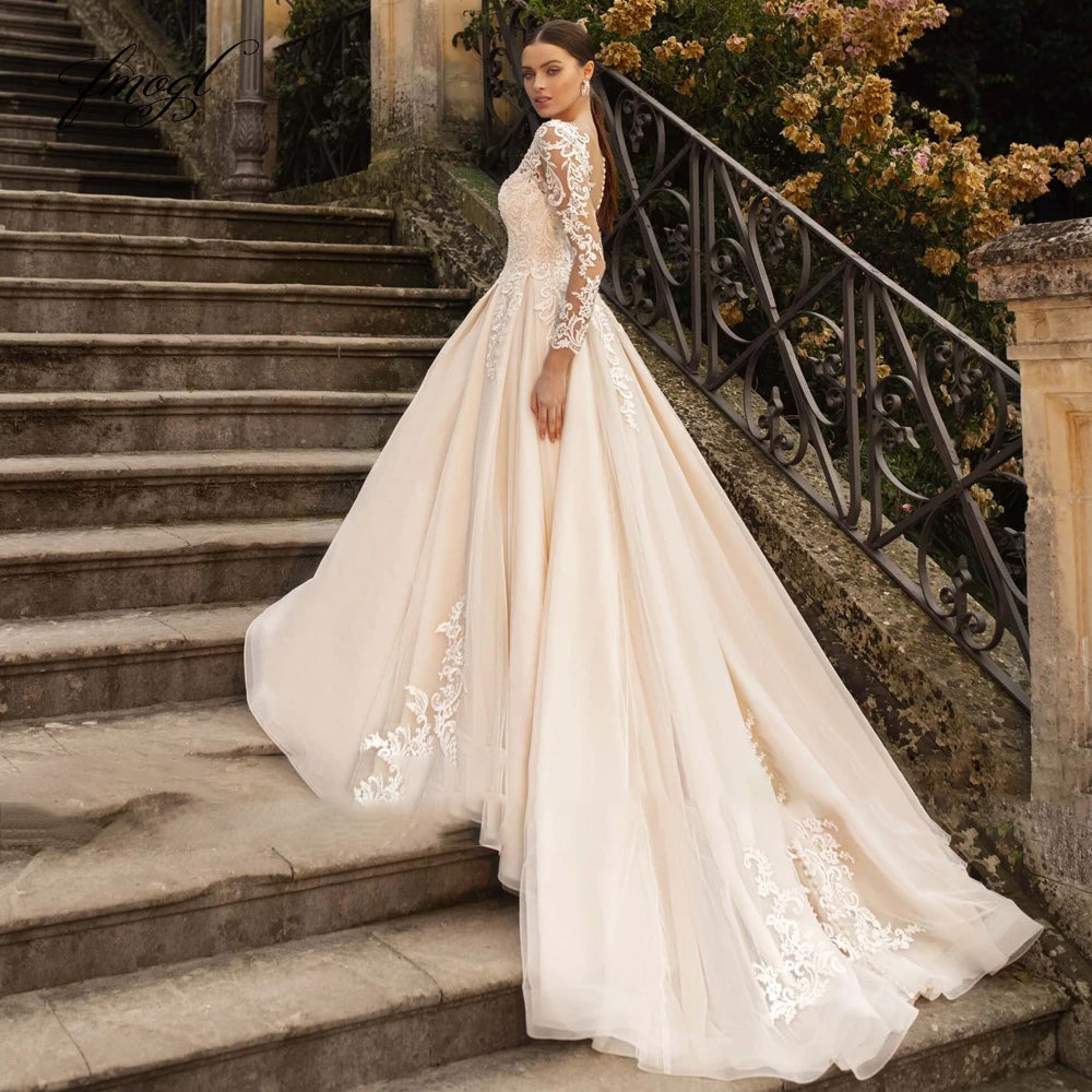 Side view of an A-line bridal gown with long lace sleeves, illusion bodice, and a flowing court train on stone steps.