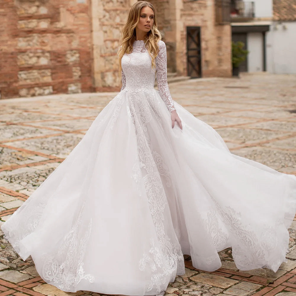 A bride wearing a luxury long sleeve lace wedding dress with a scoop neck and A-line silhouette, standing outdoors on a stone path.