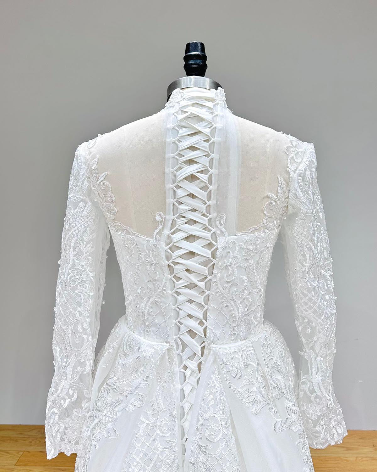Close-up back view of a luxury long-sleeve mermaid wedding dress featuring a corset lace-up closure and pearl-embellished lace details.