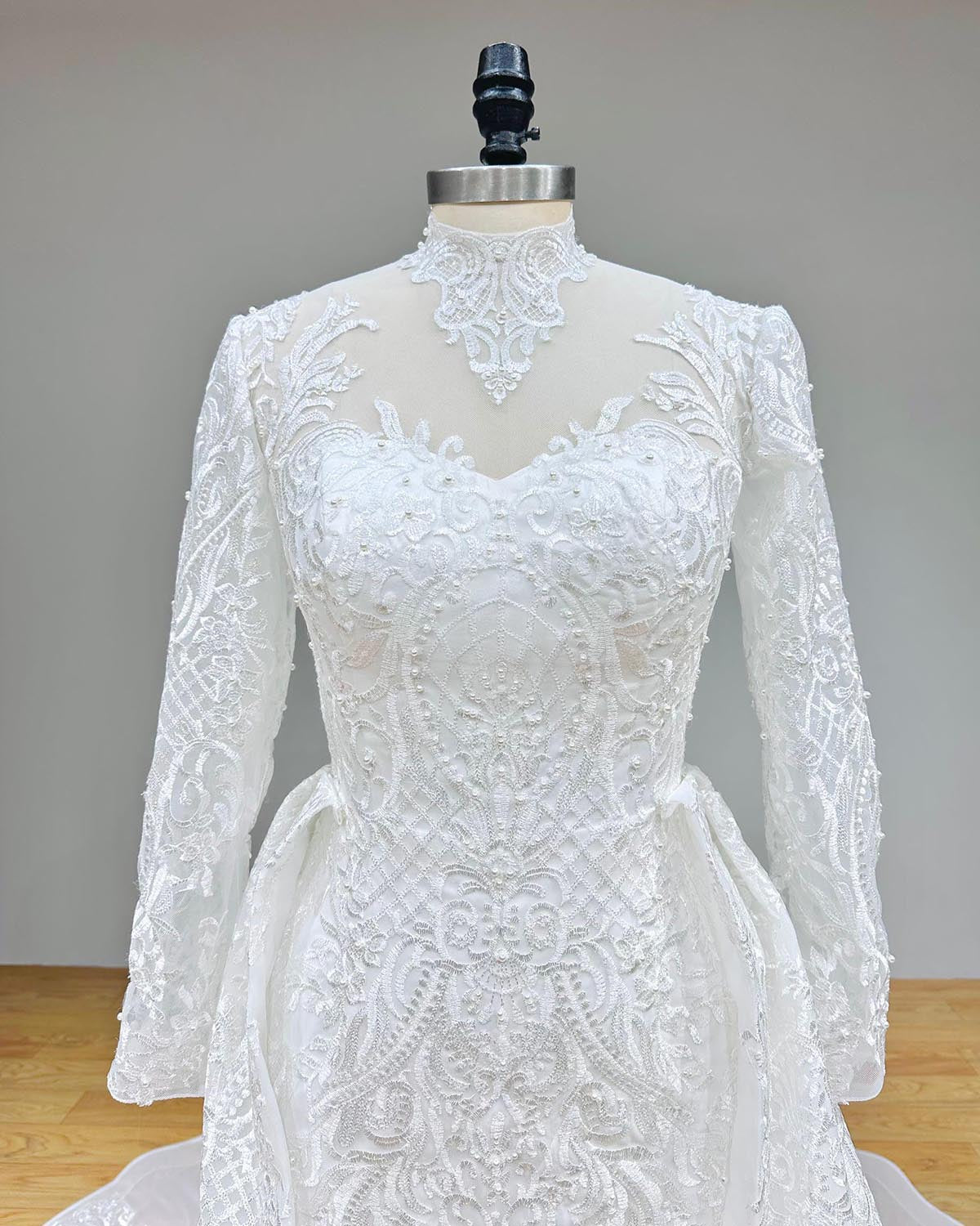 Close-up detail of the illusion high-neck bodice with intricate hand-beaded pearls and floral lace on a luxury mermaid wedding dress.