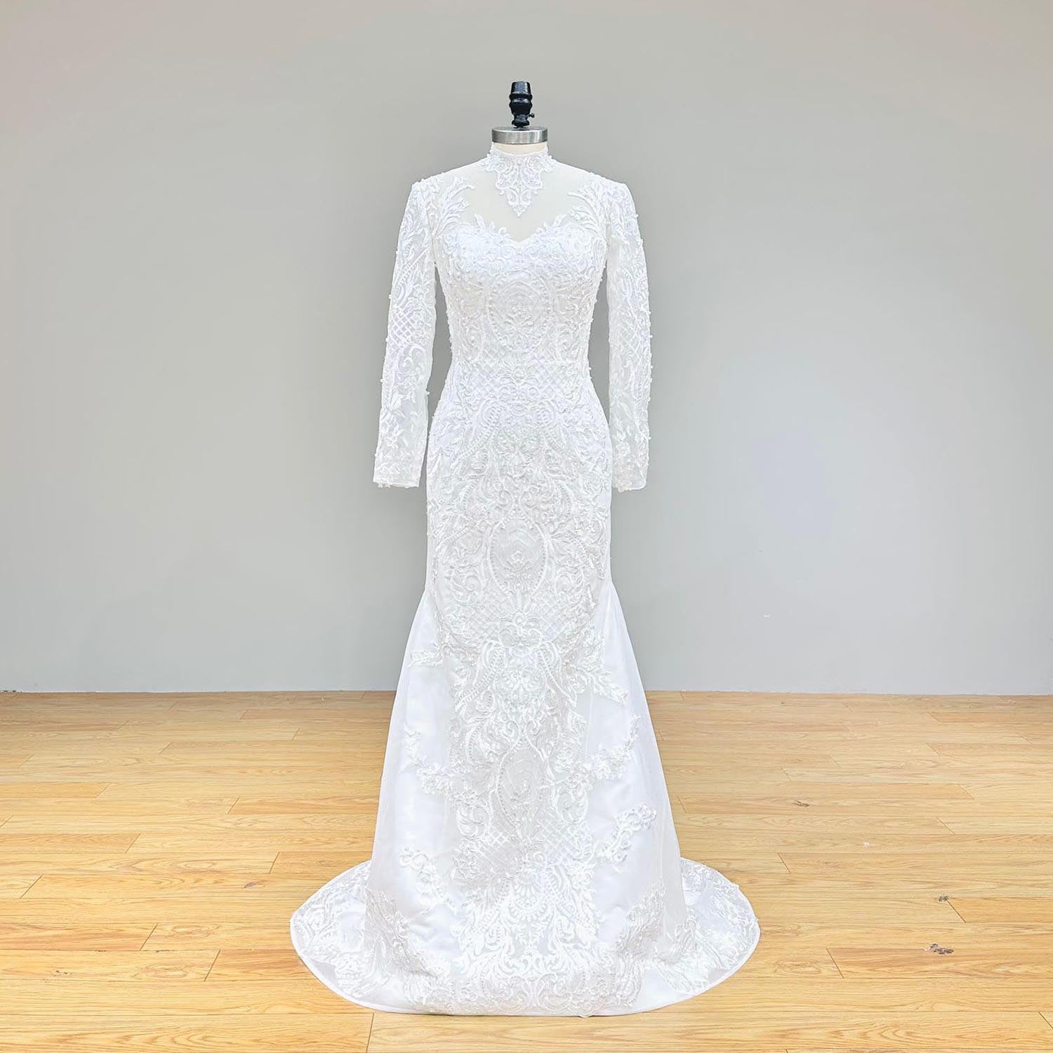 Elegant floor-length long-sleeve mermaid wedding dress with detachable skirt overlay and hand-beaded appliqués on a display mannequin.