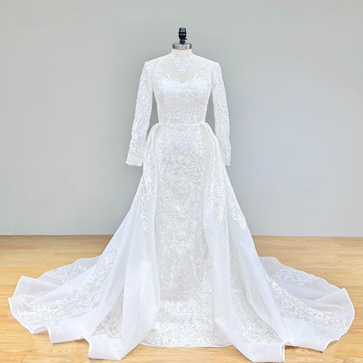 Front view of a luxurious long-sleeve mermaid wedding gown featuring a sheer high-neck bodice and beaded floral lace appliqué.