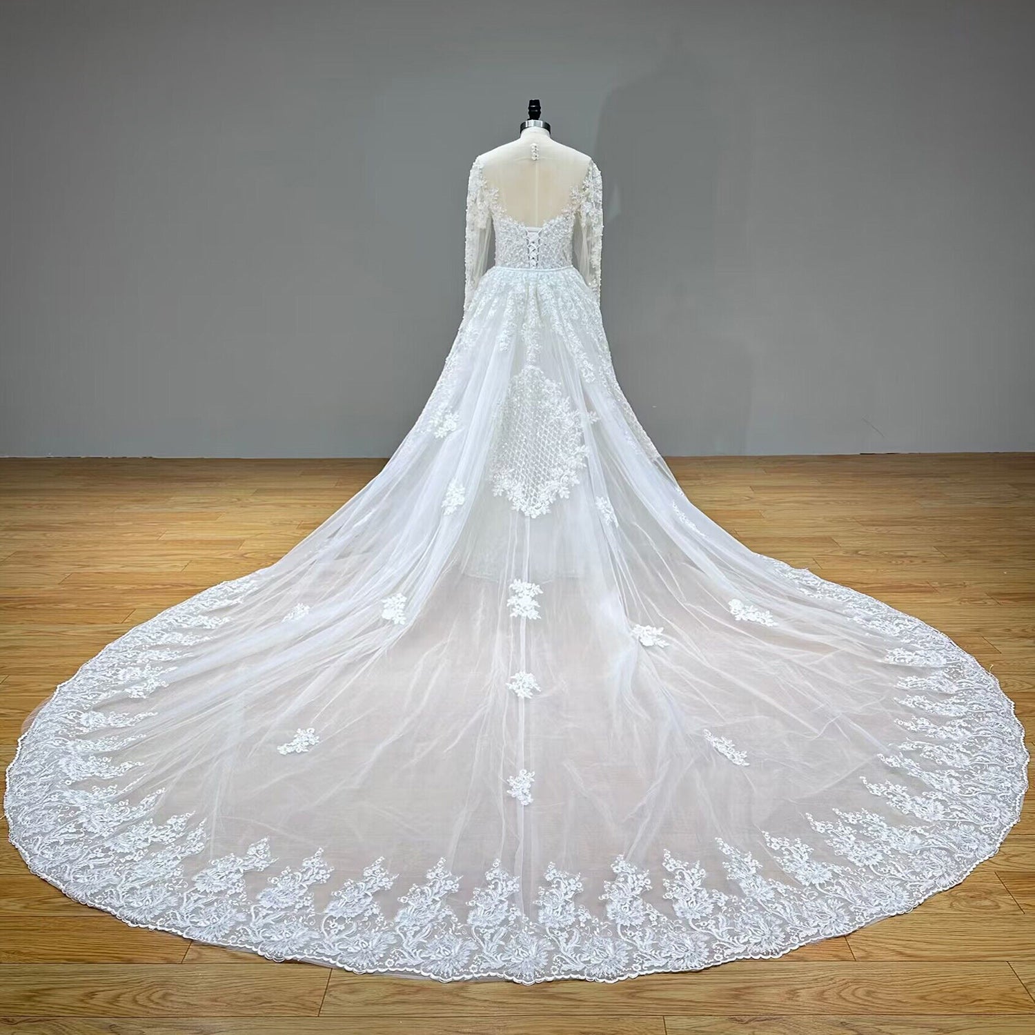 Expansive full back view of a luxury bridal gown on a mannequin, displaying the sheer illusion back, lace-up corset closure, and a sweeping detachable cathedral train with a scalloped lace border.